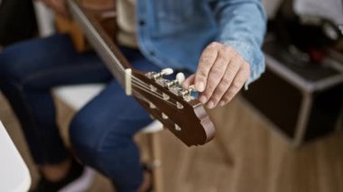 Yetişkin bir adamın akustik bir gitarı akort etmesi, ev ortamında yetenek ve konsantrasyon sergilemesi.