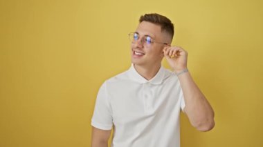 Neşeli, genç İspanyol bir adam, kendine güvenen gözlüklü, izole edilmiş sarı arka planda göze çarpıyor, parlak bir gülümsemeyi ön plana çıkarıyor, mutluluk ve güven saçıyor, büyüleyici bir şekilde gülüyor..