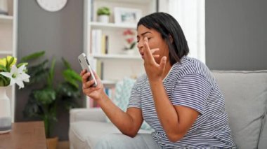 Evde çiçekli, saatli, kitaplı ve kanepeli akıllı telefon kullanan İspanyol kadın..