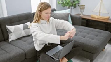 A young caucasian woman stretches while using a laptop in her modern living room.