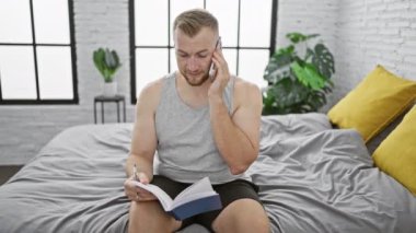 Sakallı odaklanmış genç bir adam evde bir yatakta oturur, bir deftere yazarken telefonla konuşur..