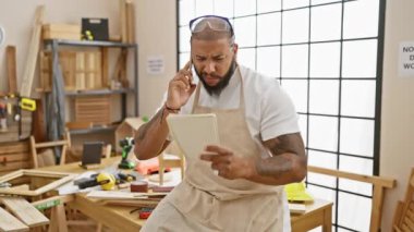 Atölyede sakallı, telefonla konuşan ve elinde defter tutan odaklanmış bir adam..