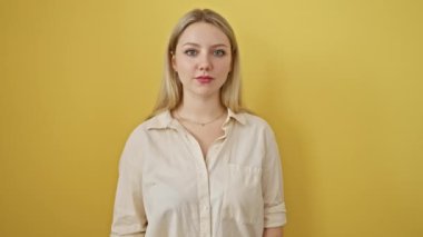 Neşeli genç sarışın kadın, sarı izole bir arka plana karşı duruyor, kendine güvenen bir gülümsemeyle havalı bir 'tamam' işareti gösteriyor, neşe, mutluluk ve başarıyı ifade ediyor.