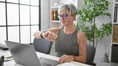 Olgun iş kadını modern ofiste çalışırken zamanı kontrol ediyor