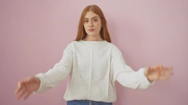 Genç kızıl saçlı kadın ayakta dikiliyor dürbün gibi jest yapıyor, gözleri parmaklarından bakıyor. Çılgın bir ifade. izole edilmiş pembe arkaplan