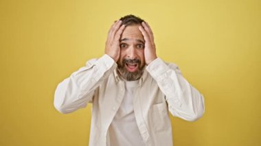 Gri saçlı olgun sakallı adam sarı arka planda şok ve kafa karışıklığı yaşıyor..