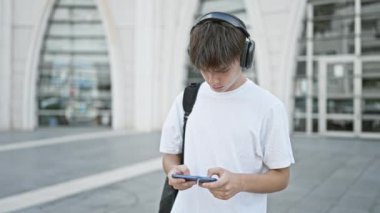 Kulaklıklı sarışın genç kampüste akıllı telefon kullanıyor..