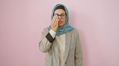 Orta yaşlı, tesettürlü İspanyol bir kadın, uykulu esneme, yüzünün yarısını kapalı, soyutlanmış pembe bir arka plan, geç saatlere kadar çalışan, yorgun bir sabah uyanması.