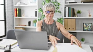 Modern ofiste dizüstü bilgisayarla çalışan olgun bir kadın.