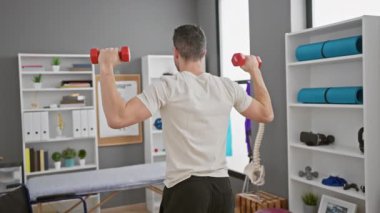 Fizik tedavi kliniğinde dambıllarla egzersiz yapan genç İspanyol bir adam..