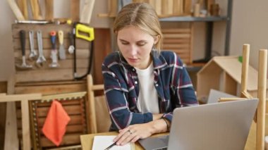 Marangozluk atölyesinde dizüstü bilgisayarda çalışan sarışın bir kadın..