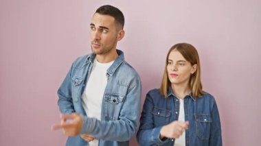 Kot gömlekli güzel bir çift, şaşkınlıktan felç olmuşlar, pembe arka planda kapalı bir yeri işaret ediyorlar.