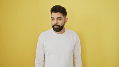 Endişeli genç adam sarı arka planda tek başına duruyor, saatleri kontrol ediyor, geç kalmaktan korkuyor.