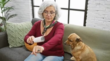 Olgun bir kadın kolunda pamuk tutarken köpek oturma odasında izliyor.