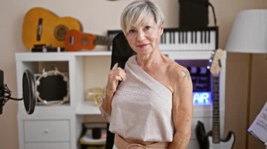 Gitarlar ve kayıt ekipmanlarıyla çevrili bir müzik stüdyosunda gri saçlı kendinden emin olgun bir kadının portresi..