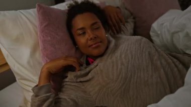 Rahat bir kadın yatak odasında rahat bir şekilde gülümsüyor, mutluluk ve rahatlık hissi uyandırıyor..