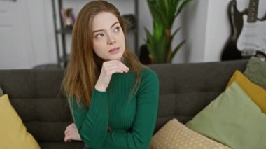 Düşünceli, genç, sarışın bir kadın, elleri çenesinde, evde şüphe dolu bir soruyla boğuşuyor, yüzünde düşünceli bir ifade var ama biraz da olsa neşe verici bir ifade.