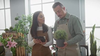 Çiçekçi dükkanında önlüklü bir adam ve kadın tablet kullanıyorlar..