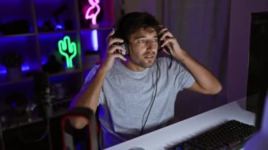 Kulaklığı olan odaklanmış bir adam geceleri neon ışıklı bir oyun odasında klavyeye takılır..