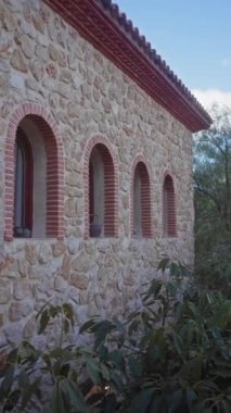 Kemerli pencereli taş bina, terracotta çatısı, gün ışığında orman yapraklarına karşı kurulmuş.