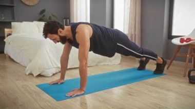 Adam yatak odasının iç kısmında yoga minderinde kalas pozisyonu alıyor, evde fitness rutinini koruyor.