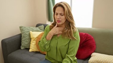 Sıkıntılı bir İspanyol kadın evinde bir koltukta oturup boğazına dokunuyor. Nefes almakta zorlanıyor ya da rahatsızlık hissediyor gibi görünüyor..