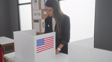 Genç bir İspanyol kadın, bir Amerikan oy kullanma merkezinde oy veriyor. Gizlilik kulübeleri ve vatanseverlik sembolleriyle..