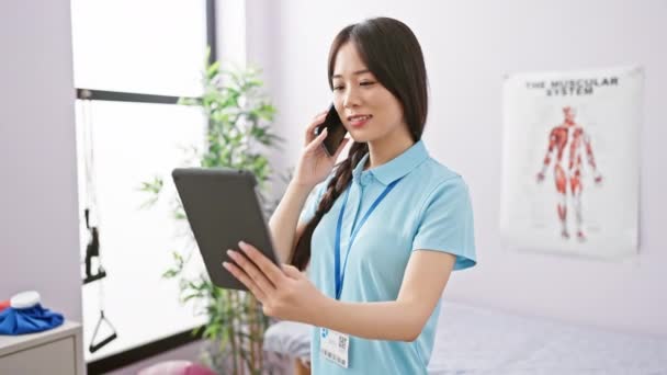 Chińska Kobieta Klinice Rozmawia Przez Telefon Trzymając Tablet — Wideo stockowe