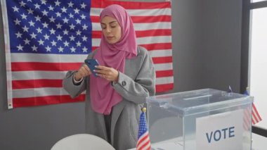 Arka planda Amerikan bayrağı olan bir oy sandığının yanında akıllı telefon kullanan Latin kökenli genç bir kadın..