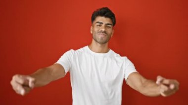 Beyaz gömlekli gülümseyen bir adam iki elini de kırmızı arka plana doğru uzatır..