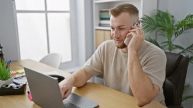 Modern bir ofis ortamında sakallı bir adam dizüstü bilgisayar ve telefonla birden fazla iş yapıyor..