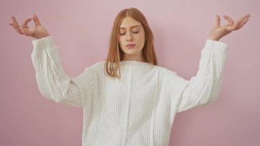 Süveter giyen güzel kızıl saçlı genç kadın Zen 'i izole edilmiş pembe arka planda, gözleri kapalı meditasyon yaparken, sıhhati kucaklarken ve yoga konseptini somutlaştırırken buluyor.