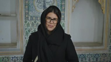 Siyah şallı, gözlüklü, gülümseyen genç bir kadın İstanbul 'daki süslü Topkapı Sarayı' nda duruyor..