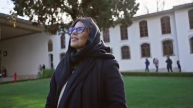 İstanbul 'daki tarihi Topkapı Sarayı' nda gözlüklü ve türban takan gülümseyen kadın, Türk kültürü ve mimarisini rahatça tecrübe ediyor..