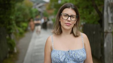 Kendine güveni tam İspanyol bir kadın, spor gözlükleri ve ciddi bir ifadeyle, onu Kyoto 'nun geleneksel sokaklarında ayakta tutuyor.