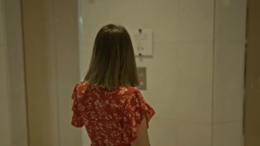 Modern otel asansöründen inen gözlüklü göz kamaştırıcı İspanyol kadın, koridorda zarif bir şekilde duruyor, genç yetişkin bir kadının iş yerindeki güzel bir portresi.