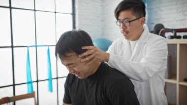 Klinikteki erkek hastanın boynunu muayene eden Asyalı doktor..