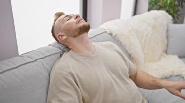 Sakallı yakışıklı genç bir adam kendini iyi hissetmiyor, evdeki bir kanepede dinleniyor..