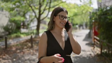 Gözlüklü güzel İspanyol kadın akıllı telefonla konuşuyor, geleneksel bir Kyoto caddesinde güven ve mutluluk yayıyor.