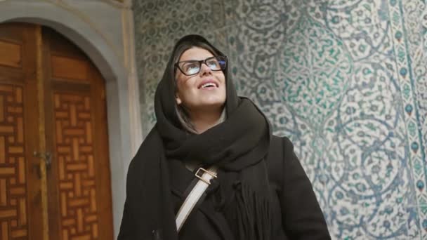 黒いスカーフの笑顔の女性は イスタンブール トルコのタイル壁に飾られたトップカピ宮殿の前に立っています — ストック動画