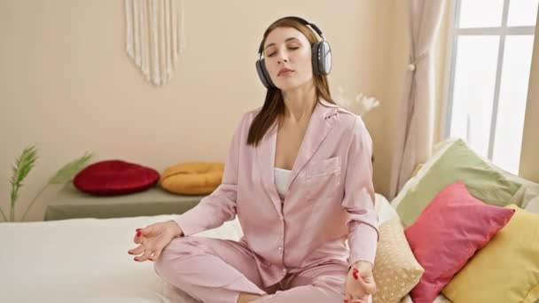 Een Vrouw Roze Pyjama Mediteert Een Bed Met Een Koptelefoon — Stockvideo