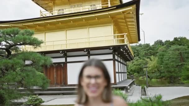 魅力的なヒスパニック女性は 彼女が笑顔で輝く喜び 息をのむようなキンカク寺の金のパビリオン 京都の宝石で彼女の眼鏡に自信とカジュアルを立っています — ストック動画