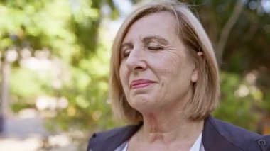 Sakin, olgun bir kadın, gözleri kapalı gülümsüyor, yemyeşil bir parkta huzur dolu bir anın tadını çıkarıyor..