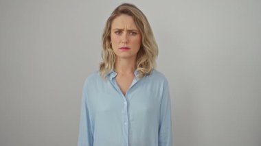 Gergin, şüpheci genç sarışın kadın hoşnutsuzluk içinde kaşlarını çatıyor. Beyaz arka planda izole edilmiş gömlek giyen bu negatif kişi sorunu somutlaştırıyor..