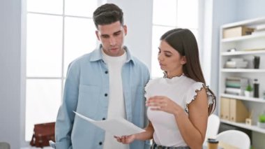 Bir erkek ve bir kadın modern bir ofiste dokümanları inceleyerek içerik hakkındaki endişelerini ve tartışmalarını dile getiriyorlar..