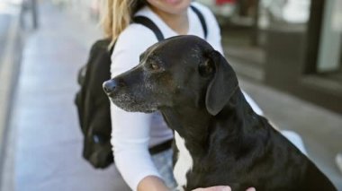 Gülümseyen bir kadın, güneşli bir şehir sokağında siyah labradorunu sevgiyle besler..