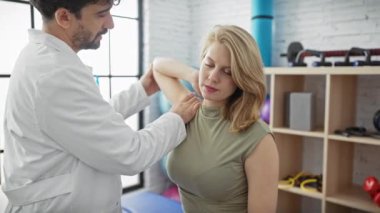 Modern bir klinikte kadının omzunu muayene eden fizyoterapist.