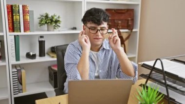 Ofisteki genç bir adam umutlarını parmaklarıyla ifade eder ve sonra dizüstü bilgisayarının önünde kitaplığa karşı sevinir..