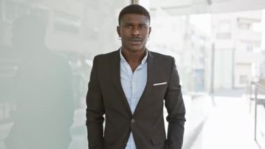 Güneşli bir şehir sokağında duran takım elbiseli kendinden emin Afrikalı bir adam.
