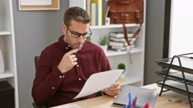 Gözlüklü, modern ofis ortamında bir belgeyi inceleyen odaklanmış İspanyol bir adam..